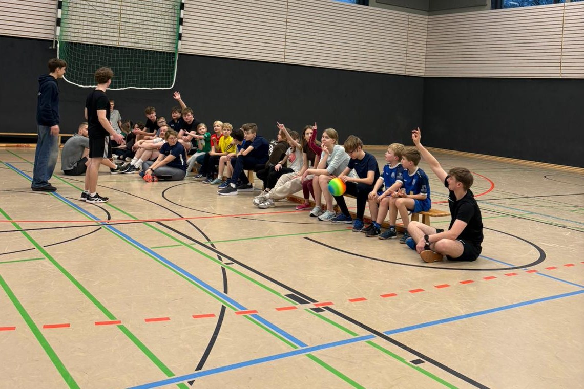 Kinder und Jugendliche sitzen in der Sporthalle und melden sich